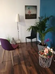Chaise violette, lampadaire, tableau et guéridon garni de pierres et de fleurs dans le cabinet