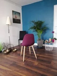 Le coin des séances individuelles : chaise violette, mur bleu canard, palmier en pot et bols tibétains posés au sol